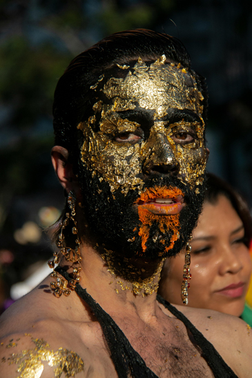 Eine Person trägt eine Maske aus Blattgold und schwarzer und orangener Farbe.